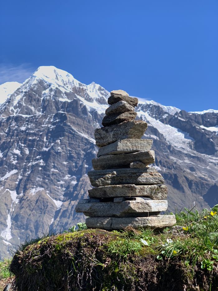 Stone cairn with a backdrop of towering snow-capped mountains under a clear sky.