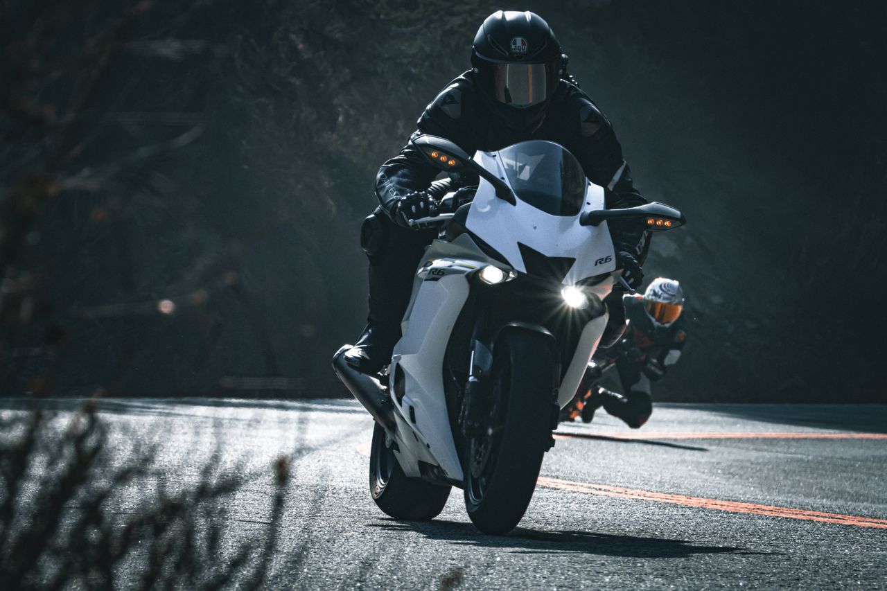 Two motorcyclists racing on a scenic curved road, showcasing speed and precision.