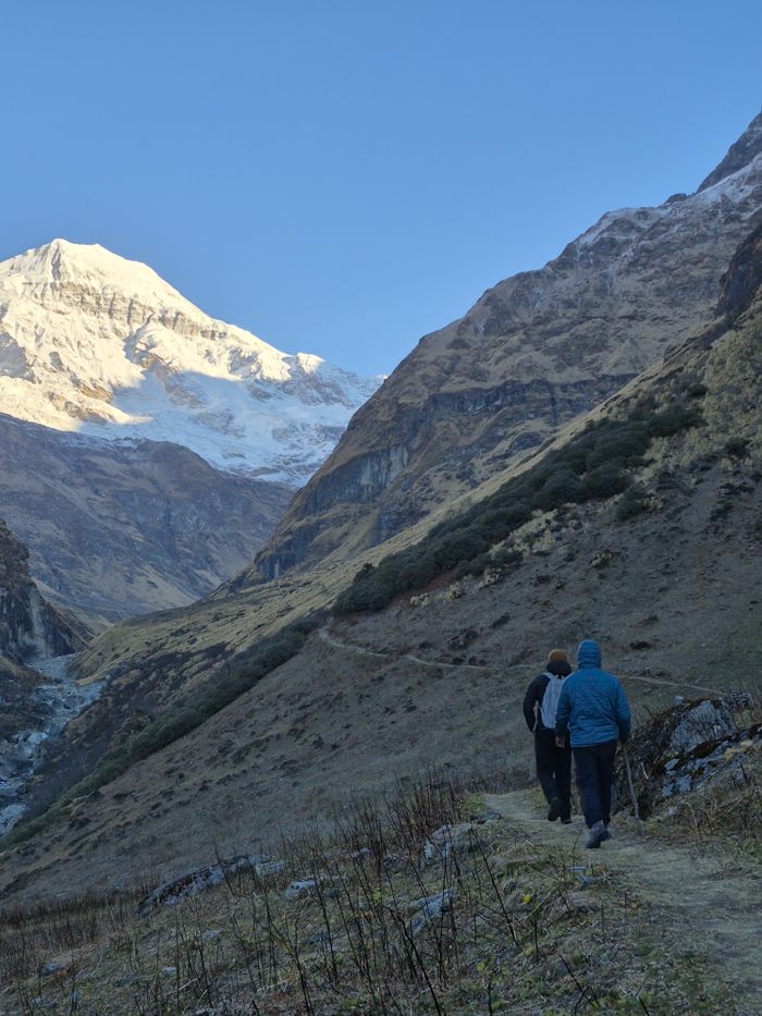 Two hikers walking along a trail amid stunning mountain scenery in the Annapurna region.