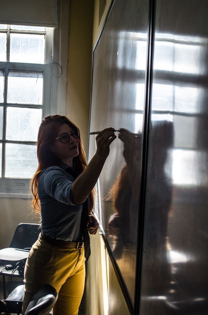 A teacher writing on a whiteboard in a sunlit Buenos Aires classroom.